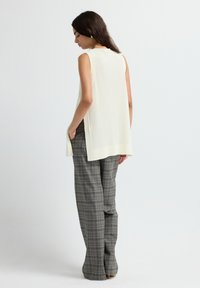 Top sin mangas de color crema con textura acanalada, que presenta aberturas laterales. Combinado con pantalones de cuadros de cintura alta en tonos gris y azul.