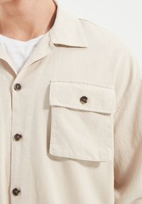 Beige overhemd met knopen gemaakt van lichte stof, met een borstzak met een knoop en een gestructureerd oppervlak.