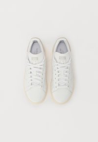 Zapatillas de cuero blanco con un acabado suave, diseño de cordones, detalles perforados y suelas de goma crema. Presenta una marca en la lengüeta.