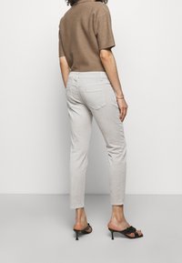 Haut en maille beige à manches courtes ; jeans gris clair ajustés avec cinq poches. Le mannequin porte des sandales noires à talons avec un détail noué.