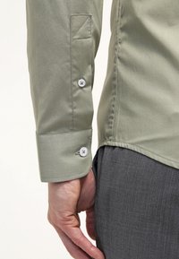 Hellgrünes, figurbetontes Langarmhemd mit glatter Textur. Verfügt über Manschetten mit Knöpfen in Weiß und einen spitzen Kragen.