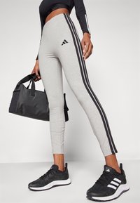 Grå leggings med svarta sidostråk, med en adidas-logotyp; matchat med en svart gymväska och svarta träningsskor med vita accenter.