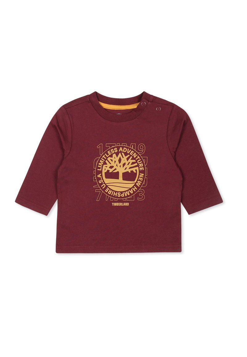 Bordowa koszulka z długim rękawem wykonana z bawełny, z żółtym wzorem graficznym drzewa i tekstem na środku, z zatrzaskami na ramieniu.