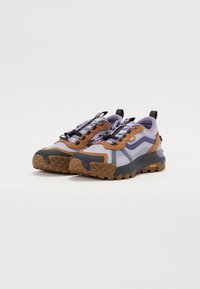 Vans tursko i lyselilla med grå og brun aksent. Mesh-overdel, teksturert gummisåle og reflekterende lisser for ekstra detaljer.