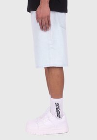 Light blue denim shorts with a straight cut, paired with white sneakers and white socks featuring black text. Simple design and casual fit.