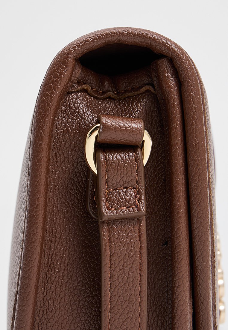 Bolso de piel marrón con un acabado texturizado, vista lateral que muestra un detalle de herrajes dorados y un asa superior asegurada por una correa.
