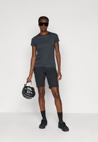 Svart treningsskjorte med korte ermer, sammen med svarte shorts. Figuren holder en svart hjelm og har på seg mørke solbriller.