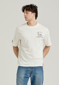 White short-sleeve t-shirt made from cotton, featuring a graphic print on the left chest and a logo on the left sleeve. Classic fit.