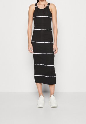 Robe débardeur noire avec des rayures blanches en tie-dye, silhouette ajustée, longueur au genou, fabriquée en tissu extensible, assortie à des baskets blanches.