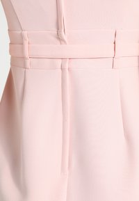 Gros plan sur un tissu rose clair montrant une ceinture avec des passants et une ceinture assortie passant à travers eux.