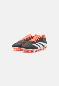 Scarpe da calcio nere con accenti e lacci arancioni. Presentano strisce bianche e una superficie testurizzata. Suola con tacchetti per una migliore trazione.