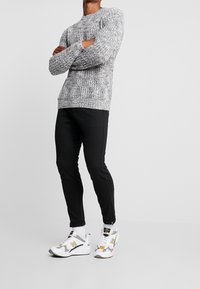 Grau-weißes strukturiertes Strickpullover, kombiniert mit schwarzen schmal geschnittenen Hosen und weißen Sneakers mit grauen und gelben Akzenten.