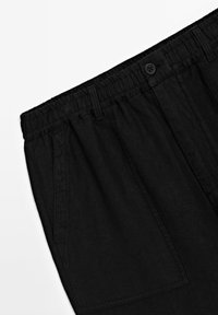 Pantalons en lin noirs avec une taille élastique, poches avant et fermeture à un bouton. Texture lisse et coupe décontractée.