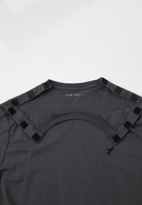 Σκούρο γκρι T-shirt με στρογγυλή λαιμόκοψη, που διαθέτει λεπτομέρεια με κομμένο σχέδιο στην πλάτη και μικρές μαύρες τετράγωνες λεπτομέρειες στους ώμους.