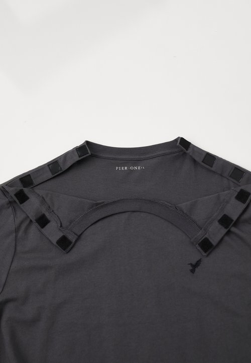 Camiseta gris oscuro con escote redondo, que presenta un detalle de corte con bucle en la parte posterior y pequeños acentos cuadrados negros en los hombros.