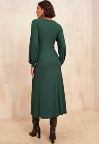 Rochie maxi verde cu dungi, cu mâneci lungi puff și talie ajustată, asortată cu cizme negre cu toc până la genunchi. Textura este netedă și structurată.