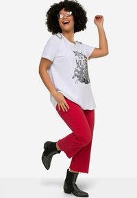 Hvid t-shirt med en zebra grafik og teksten "Born to be Wild", parret med røde cropped bukser og sorte nitter ankelstøvler.