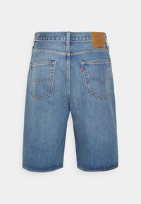 Shorts en denim bleu à coupe droite, avec deux poches arrière et un patch en cuir beige sur la ceinture. Présente un léger effet délavé et des détails de couture.