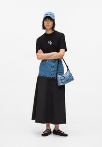Tricou grafic negru, fustă din denim cu tiv detasat, și o geantă din denim albastru. Accesoriile includ o șapcă albastră deschisă și pantofi negri.