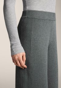 Sivý rebrovaný top s dlhým rukávom spárovaný s tmavosivými elastickými nohavicami s voľným strihom, ktoré majú hladkú textúru a vysoký pás.