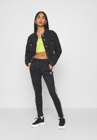 Svart denimjacka, neongrön crop top, svarta träningbyxor med vita ränder och svarta sportskor med en tjock sula.