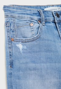 Svetlo modre kavbojke iz jeansa z uničenim žepom in manjšim raztrganim detajlom. Imajo gumbasto zapiranje in bakrene zakovice.