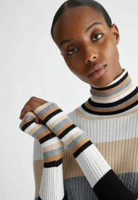 Maglione a collo alto lavorato a maglia con righe verticali e orizzontali in crema, beige, grigio e nero; presenta una texture a coste e maniche senza dita.