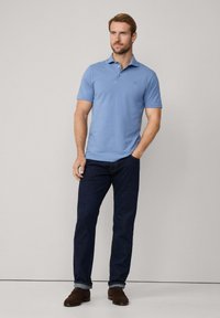 Gai zils polo krekls ar klasisko apkakli, apvienots ar tumšiem džinsiem. Audums izskatās gluds, ar īsām piedurknēm. Brūni apavi noslēdz izskatu.