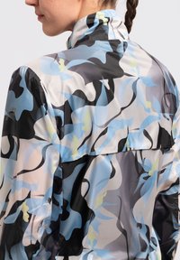 Chaqueta ligera con un patrón que presenta diseños abstractos en negro, azul y amarillo pálido, con un cuello estructurado y un acabado de tela texturizada.