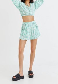 Jasnozielony kwiatowy krótki top z wiązaniem, zestawiony z pasującymi szortami z kieszeniami. Całość dopełniają czarne sandały na platformie.