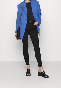 Modrý oversize blazer, černé přiléhavé tričko, černé úzké džíny, černé otevřené lodičky na podpatku. Hladká tkanina a strukturovaný design.