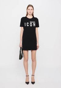 Zwarte katoenen T-shirt jurk met vetgedrukte witte tekst "DSQUARED2 ICON", korte mouwen en een rechte snit. Gecombineerd met een gestructureerde groene tas.