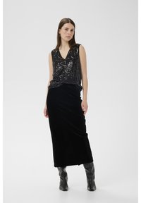 Juodas blizgančiais siūtais viršus su V formos iškirpte, derinamas su juoda aksomine suknele. Modelis dėvi blizgius pilkus iki kelių siekiančius batus. Minimalistinė fono aplinka.