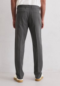 Graue Hose mit geradem Schnitt, ausgestattet mit Gesäßtaschen und glatter Textur. Kombiniert mit weißen Schuhen und neutralem Hintergrund.