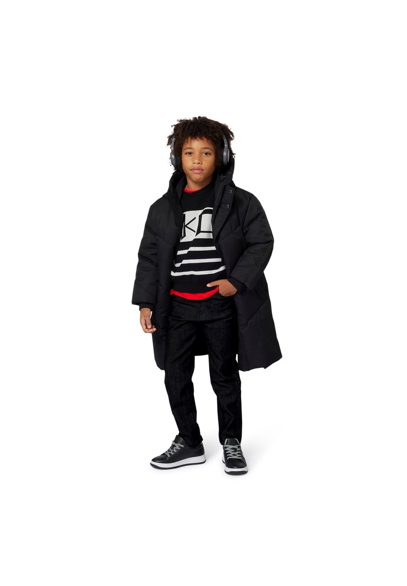 Juodas paminkštintas paltas su gaubtu, dėvimas ant juodos ir baltos dryžuotos megztinio, raudonos marškinėlių ir tamsių džinsų. Juodi sportbačiai ir ausinės.