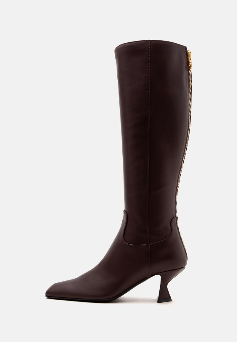 Botte en cuir marron foncé montant jusqu’au genou, bout pointu, fermeture éclair dorée à l’arrière et talon moyen effilé, vue de côté sur fond blanc.