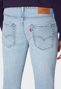 Jeans de denim azul claro con un corte recto, bolsillos traseros con costuras distintivas y una etiqueta de parche de cuero en la cintura.