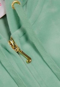 Fleece verde menta con zip, dotato di accessori dorati, presenta un tirazip testurizzato e un cordino abbinato. Tessuto morbido e liscio.