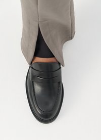 Black leather shoe with a rounded toe, smooth texture, and a decorative band across the front. Worn with beige pants.
