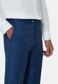 Blauwe dresspants gemaakt van een gestructureerde stof, met een vlakke voorkant, zijzakken en een knoopsluiting. Gecombineerd met een witte shirt met lange mouwen.
