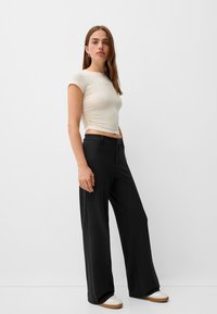 Beige fitted short-sleeve top paired with high-waisted black wide-leg pants and white sneakers, set against a plain background.