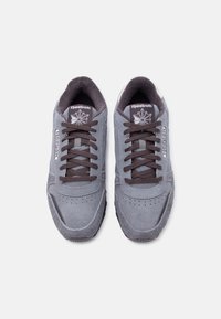 Ζευγάρι γκρι αθλητικά παπούτσια Reebok με μαύρα κορδόνια, σουέντ υφή και λογότυπο στη γλώσσα και στο πλάι, εμφανιζόμενα από πάνω σε λευκό φόντο.