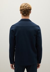 Giacca blu navy con colletto, realizzata in tessuto morbido, presenta una vestibilità dritta e polsini abbottonati. Design semplice senza motivi o accenti.