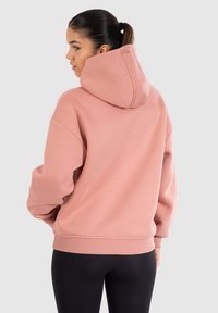 Sweatshirt à capuche rose avec une coupe décontractée, des poignets et un ourlet côtelés, et une texture lisse et douce. Caractérisé par une capuche oversize.