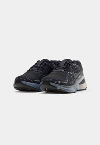 Zapatillas de correr con parte superior de malla negra que presenta manchas blancas, una media suela acolchada y una suela exterior de goma reforzada.