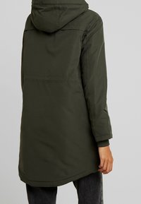 Mörkgrön vadderad jacka med huva, i en midjelång design och elastiska manschetter. Slät struktur med en minimalistisk stil.