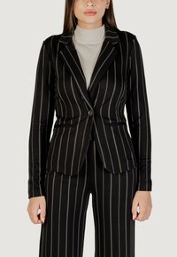 Černý pruhovaný blazer se zelenými proužky, jednobuttonová zapínání, dvě přední kapsy, přiléhavý střih, hladká tkanina, nošený přes světle béžový rolák.