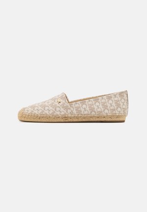 Alpargata beige sin cordones con suela de yute trenzado y patrón general en beige claro con letras estilizadas, además de un pequeño logo dorado en la parte superior.