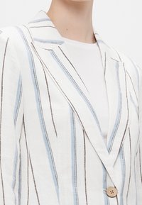 Linen blazer featuring vertical blue and brown stripes on a white background. Notable details include a single button closure and notch lapel.