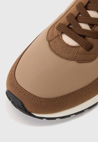 Brown athletic shoe featuring a smooth upper with suede accents, lace closures, and a black rubber outsole. Tread detail visible.